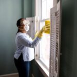 Weekly Cleaning - woman in white long sleeve shirt and blue denim jeans standing beside white wooden framed glass