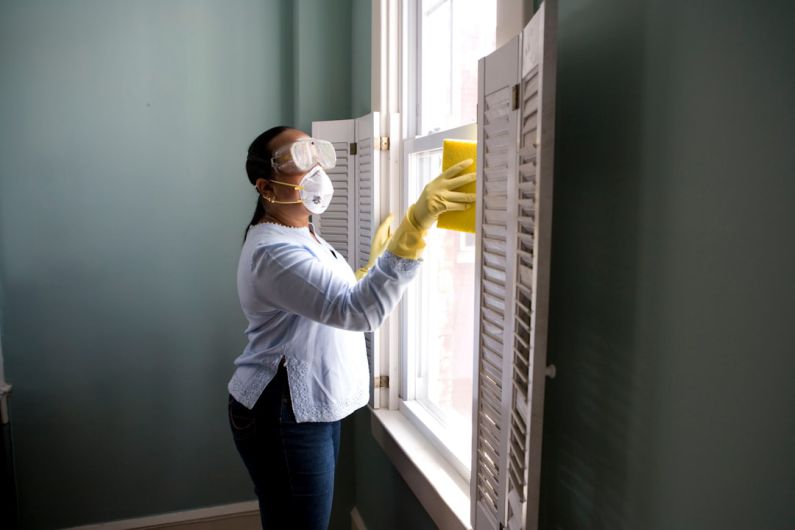 Weekly Cleaning - woman in white long sleeve shirt and blue denim jeans standing beside white wooden framed glass